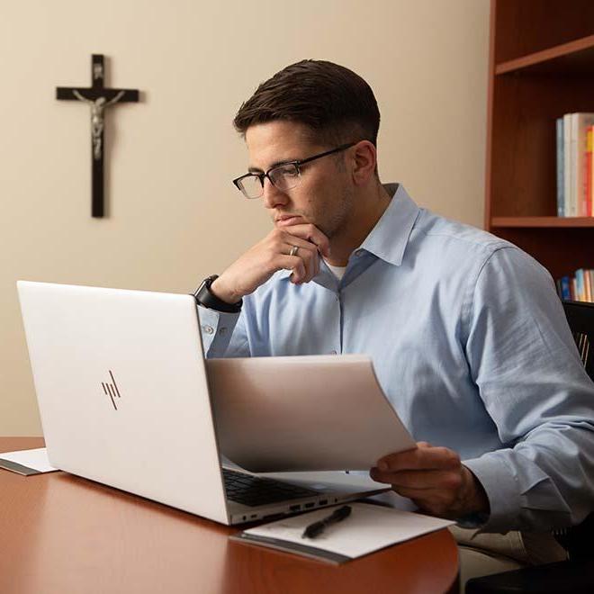 年轻的专业人员在笔记本电脑上工作，背景是十字架